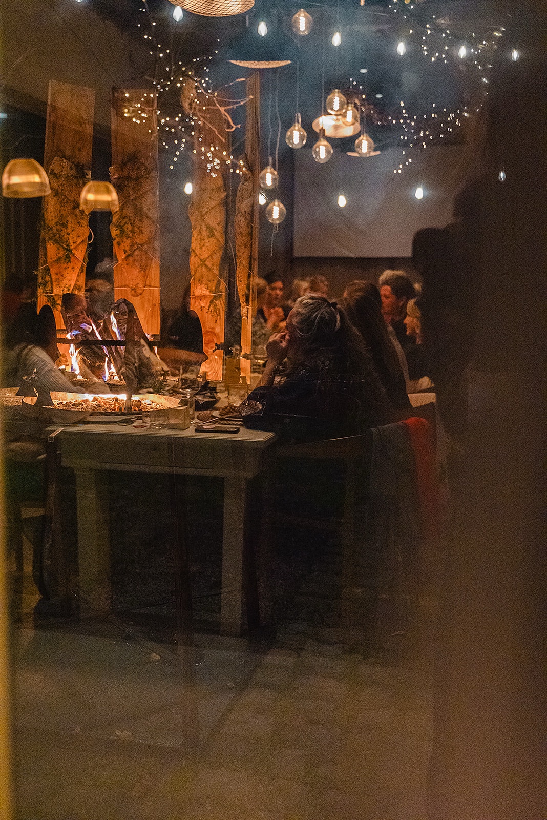 Gasten genieten 's avonds van een feestelijk diner bij het vuur, met lichtjes in de bomen